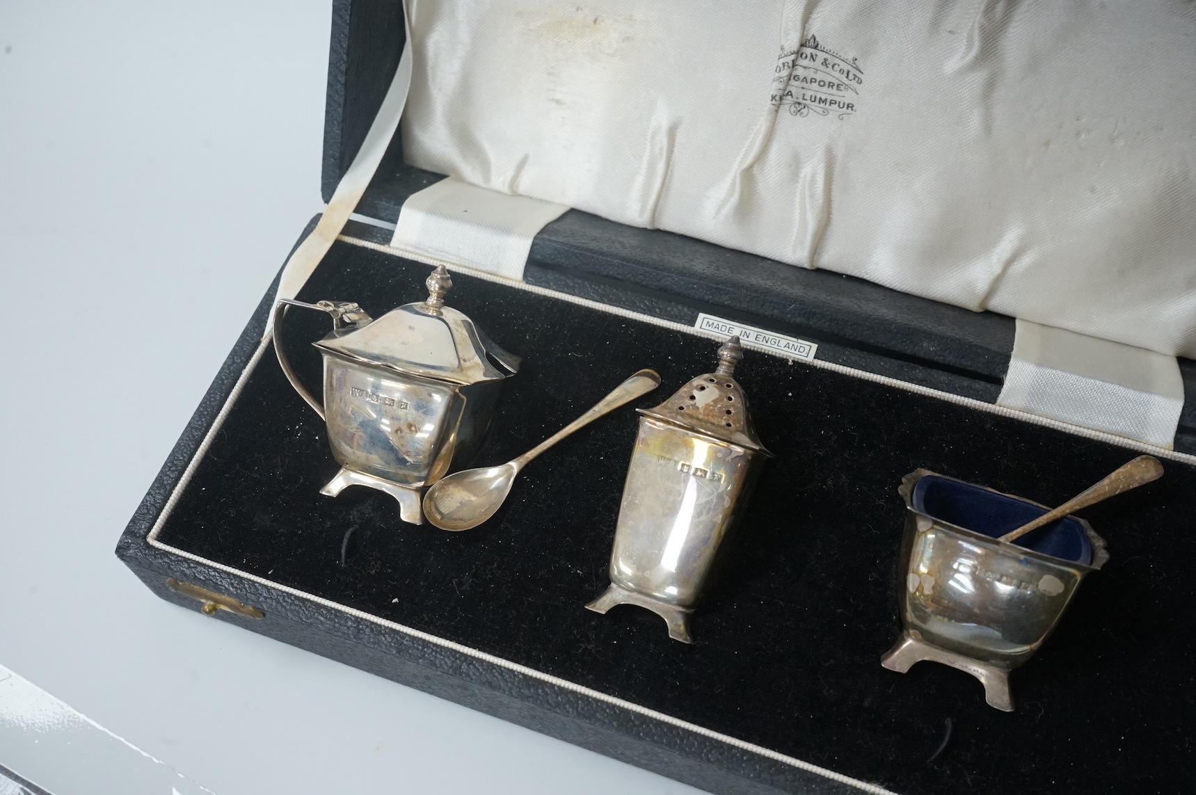 A pair of cased Elizabeth II silver three piece condiment sets, by William Adams Ltd, Birmingham, 1955, one spoon missing.
